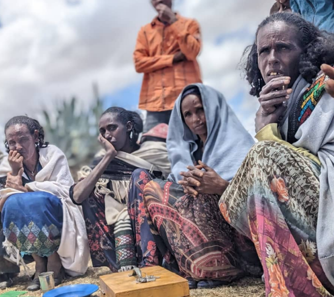 Four Ethiopian villagers crouch on the ground in a line with concerned faces.