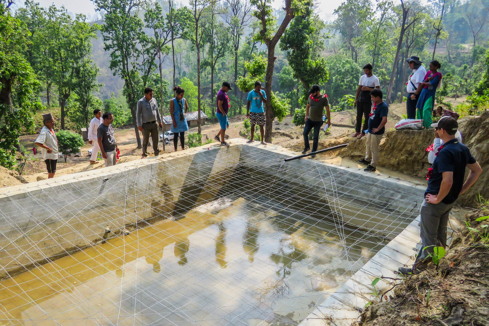 Representatives from USAID Nepal, IWMA, and USAID implementing partners gather with local villagers around a soil cement tank under construction by PAHAL during a group field visit to Milan Debari village, in the Rangun Khola watershed. Photo Credit: Liz Kendall