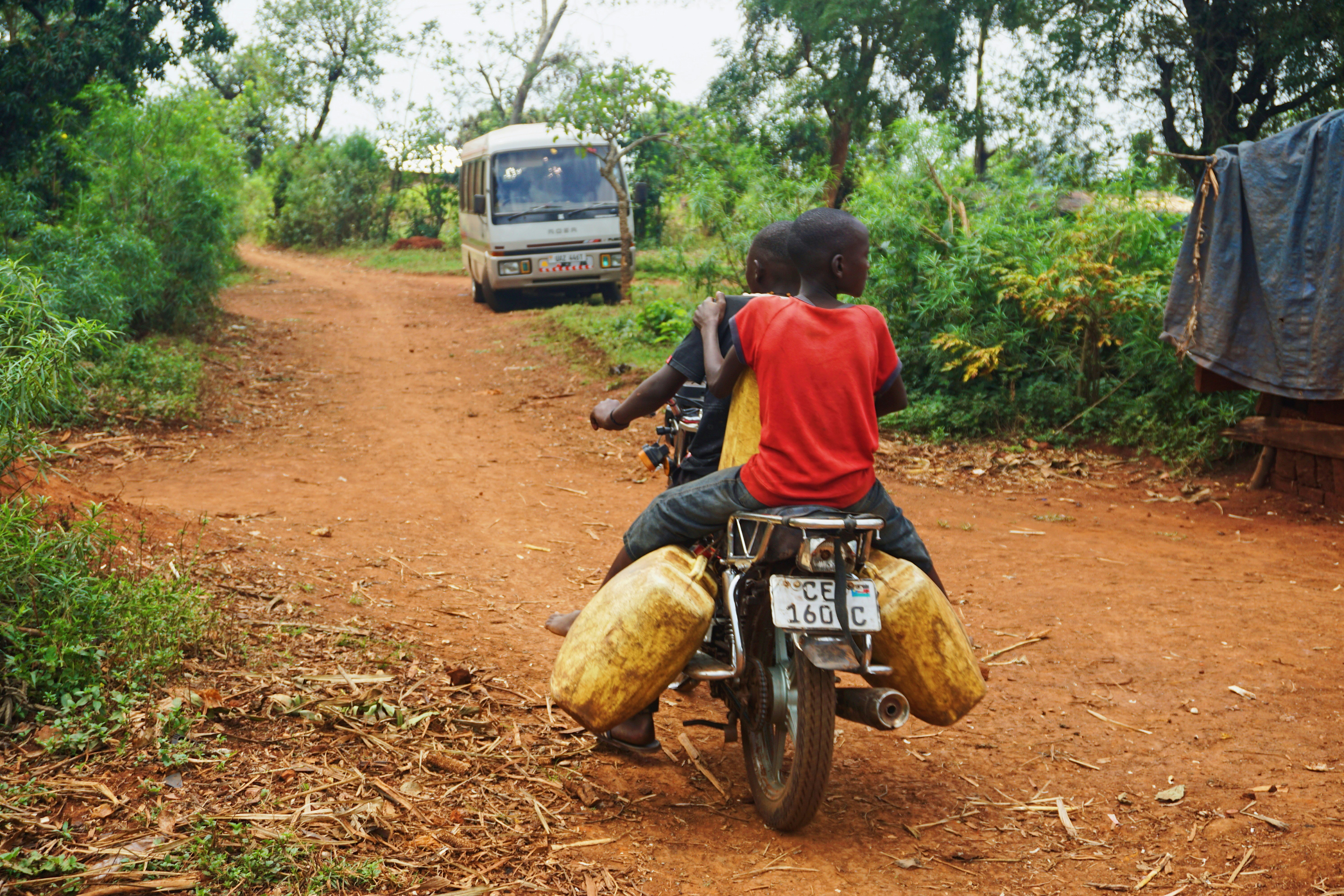 two young adults ride a motorbike down a dirt road carrying bags of supplies