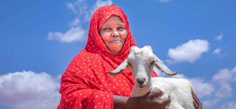 Ethiopian woman in red traditional clothing smiles while holding a goat