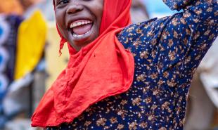 child wearing a head scarf smiles and waves at camera