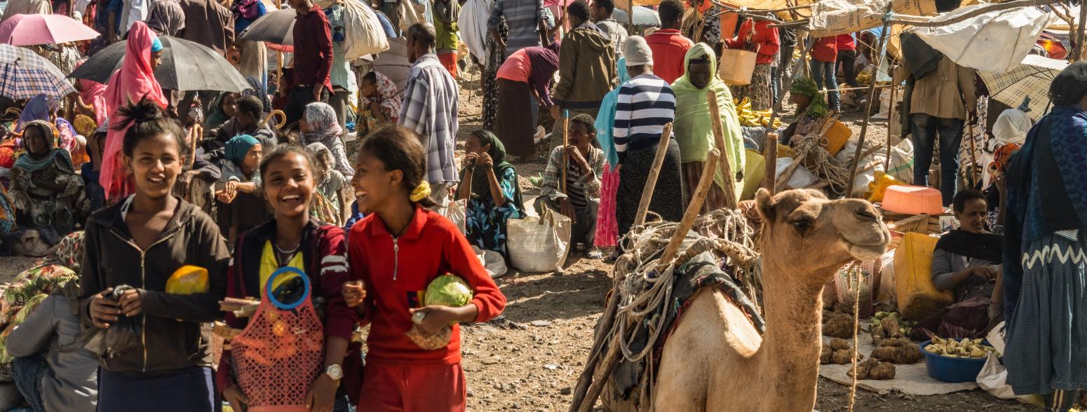 busy Ethiopian market with a camel and laughing young women